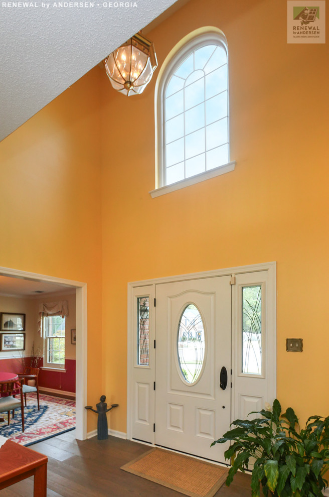 Esempio di una porta d'ingresso di medie dimensioni con pareti gialle, pavimento in legno massello medio, una porta singola, una porta bianca, pavimento marrone e soffitto a volta