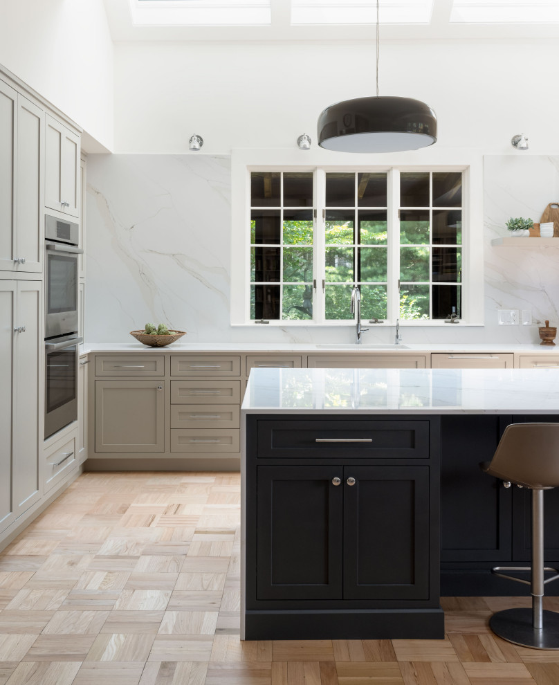 Example of a large transitional light wood floor eat-in kitchen design with an undermount sink, recessed-panel cabinets, gray cabinets, quartz countertops, white backsplash, quartz backsplash, stainless steel appliances, an island and white countertops