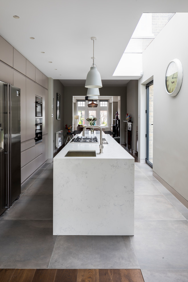 This is an example of a mid-sized contemporary single-wall open plan kitchen in London with an undermount sink, flat-panel cabinets, grey cabinets, quartzite benchtops, yellow splashback, stainless steel appliances, porcelain floors, with island and grey floor.