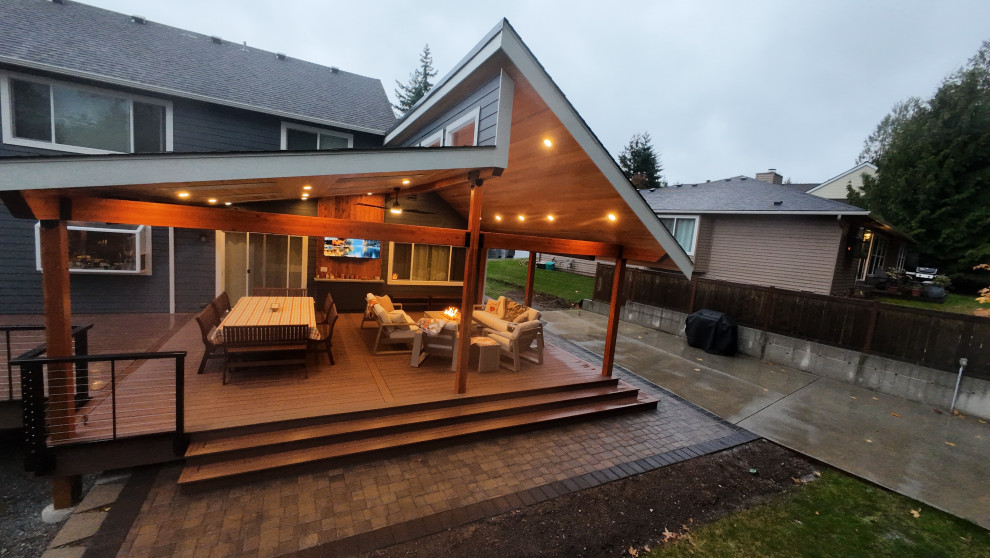 Example of a large arts and crafts backyard ground level cable railing deck design in Seattle with a fire pit and a roof extension