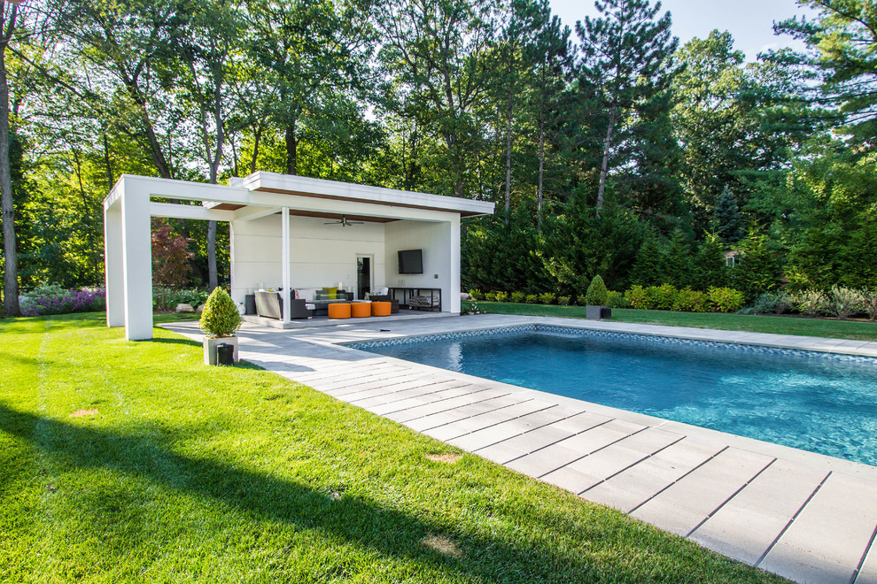 Photo of a large modern backyard rectangular pool in New York with a pool house and natural stone pavers.