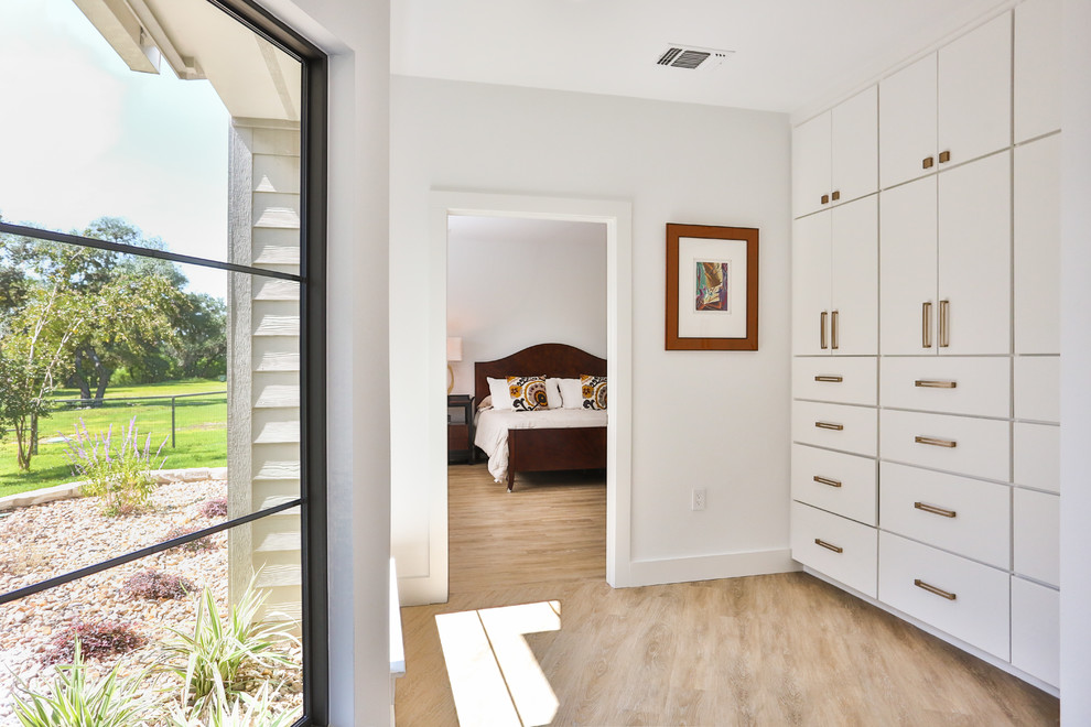 Photo of a mid-sized midcentury gender-neutral walk-in wardrobe in Austin with flat-panel cabinets, white cabinets, light hardwood floors and beige floor.
