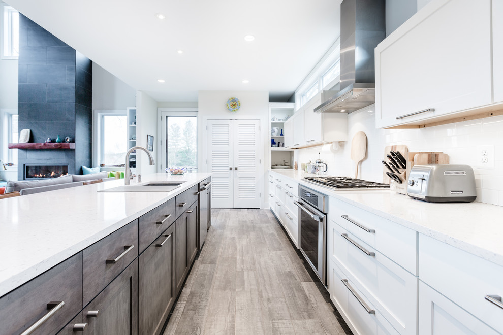 This is an example of a mid-sized contemporary l-shaped open plan kitchen in DC Metro with an undermount sink, shaker cabinets, white cabinets, quartz benchtops, white splashback, subway tile splashback, stainless steel appliances, porcelain floors, with island, grey floor and white benchtop.