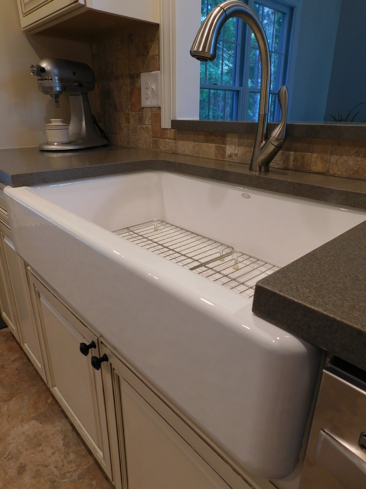 Mid-sized transitional galley vinyl floor enclosed kitchen photo with a farmhouse sink, raised-panel cabinets, beige cabinets, solid surface countertops, multicolored backsplash, stone tile backsplash, stainless steel appliances and no island