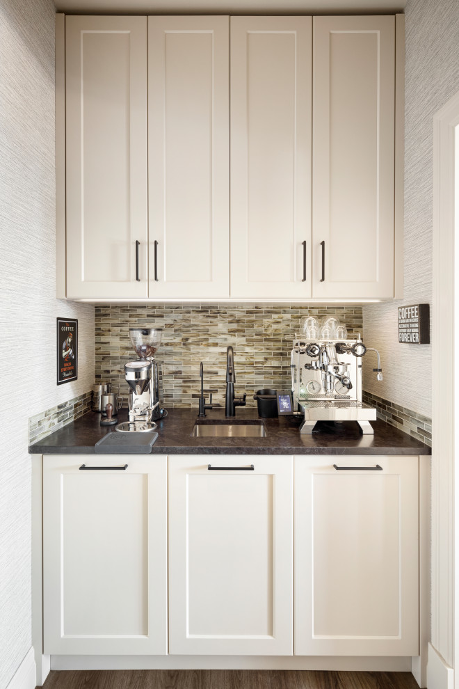 Inspiration for a large traditional galley home bar in Calgary with recessed-panel cabinets, white cabinets, granite worktops, grey splashback, glass tiled splashback, medium hardwood flooring, brown floors and black worktops.