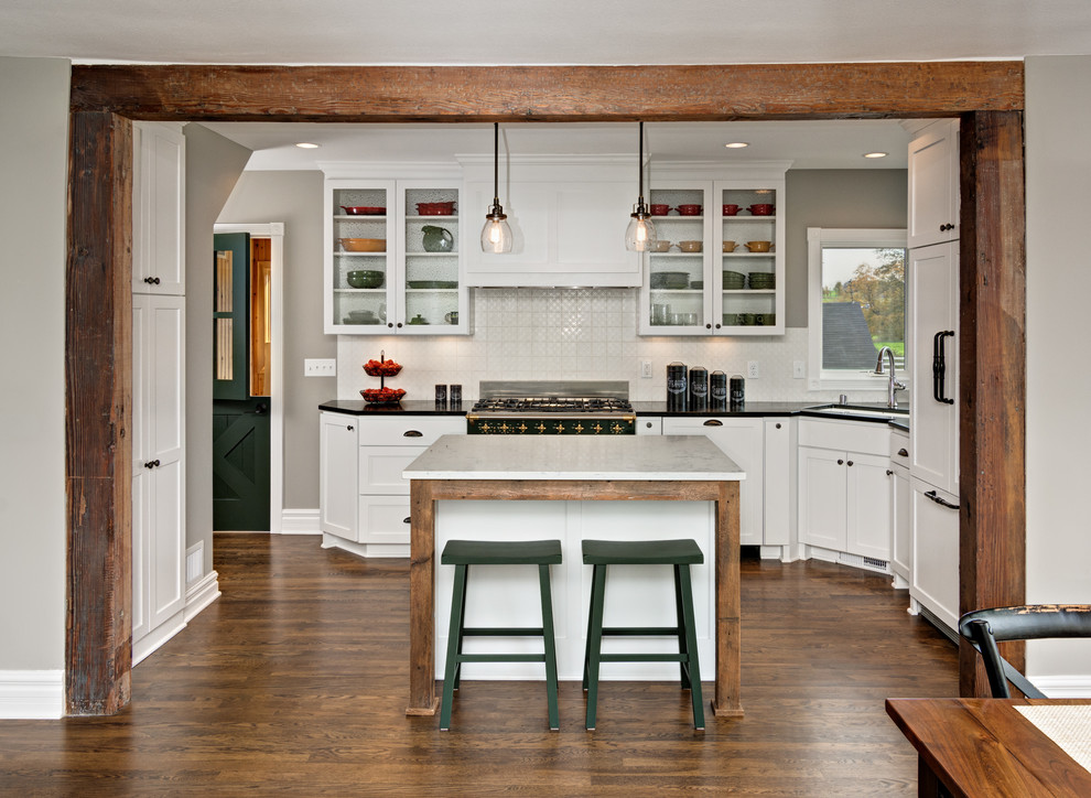 This is an example of a mid-sized country l-shaped open plan kitchen in Minneapolis with an undermount sink, shaker cabinets, white cabinets, white splashback, dark hardwood floors, with island, soapstone benchtops, ceramic splashback and panelled appliances.