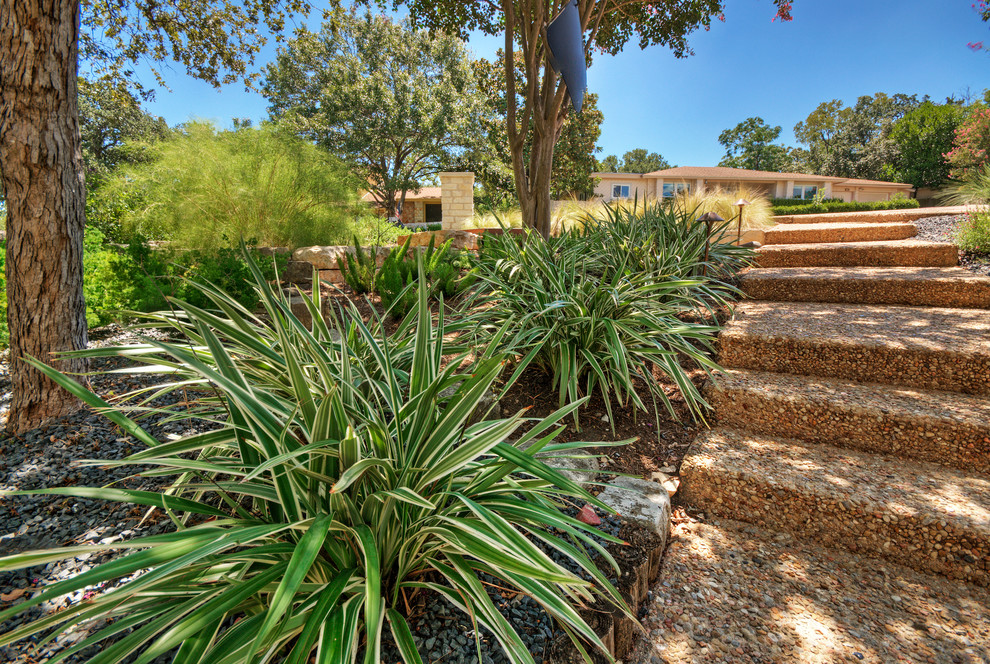 Large modern front yard shaded xeriscape in Austin with a retaining wall and gravel for spring.