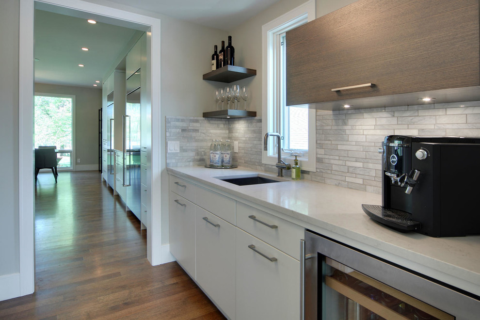 Example of a transitional medium tone wood floor and brown floor kitchen design in Calgary with an undermount sink, flat-panel cabinets, quartz countertops, gray backsplash, marble backsplash, stainless steel appliances and an island