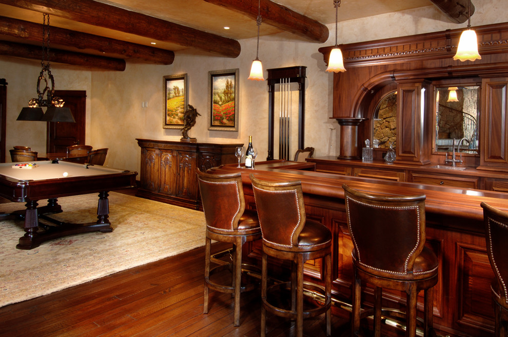 Photo of a large country seated home bar in Denver with an undermount sink, raised-panel cabinets, dark wood cabinets, copper benchtops, dark hardwood floors, mirror splashback and brown floor.