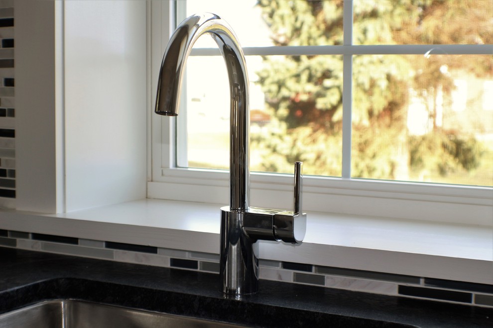 Small trendy single-wall medium tone wood floor open concept kitchen photo with an undermount sink, recessed-panel cabinets, white cabinets, granite countertops, gray backsplash, glass tile backsplash, stainless steel appliances and a peninsula