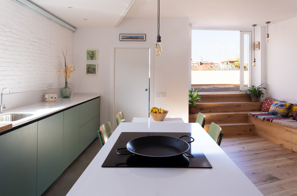 This is an example of a mid-sized contemporary single-wall open plan kitchen in Barcelona with a single-bowl sink, flat-panel cabinets, green cabinets, quartz benchtops, white splashback, brick splashback, panelled appliances, medium hardwood floors, with island and white benchtop.
