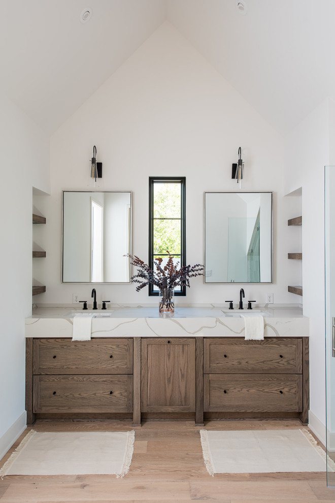Photo of a modern master wet room bathroom in Indianapolis with shaker cabinets, medium wood cabinets, a freestanding tub, white walls, light hardwood floors, an undermount sink, engineered quartz benchtops, brown floor, a hinged shower door, white benchtops, an enclosed toilet, a double vanity and a built-in vanity.