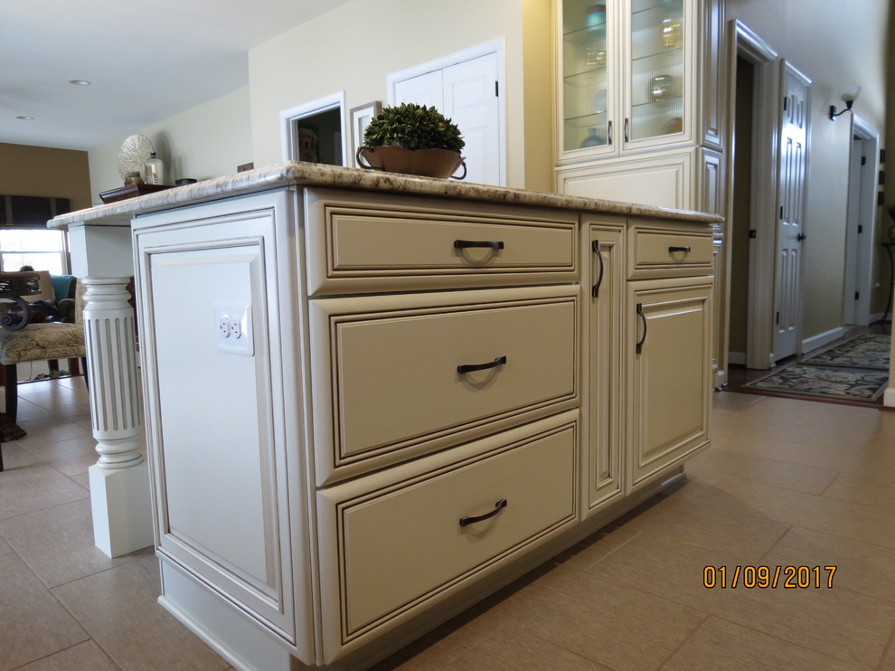 Example of a mid-sized transitional l-shaped ceramic tile eat-in kitchen design with an undermount sink, raised-panel cabinets, distressed cabinets, granite countertops, white backsplash, porcelain backsplash, stainless steel appliances and an island