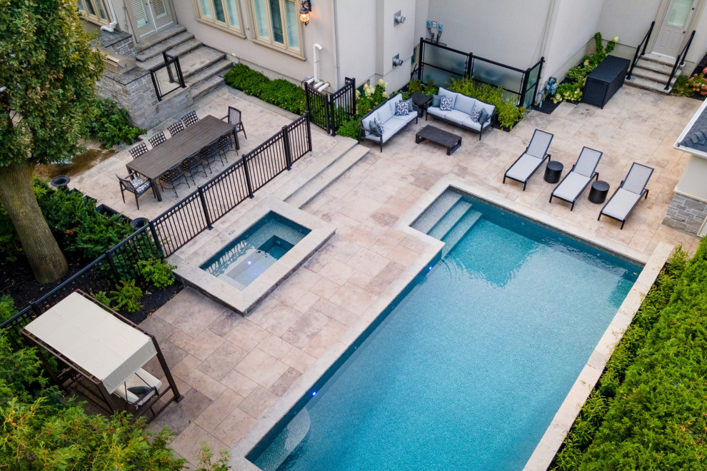Modelo de piscina clásica renovada de tamaño medio rectangular en patio trasero con paisajismo de piscina y suelo de hormigón estampado