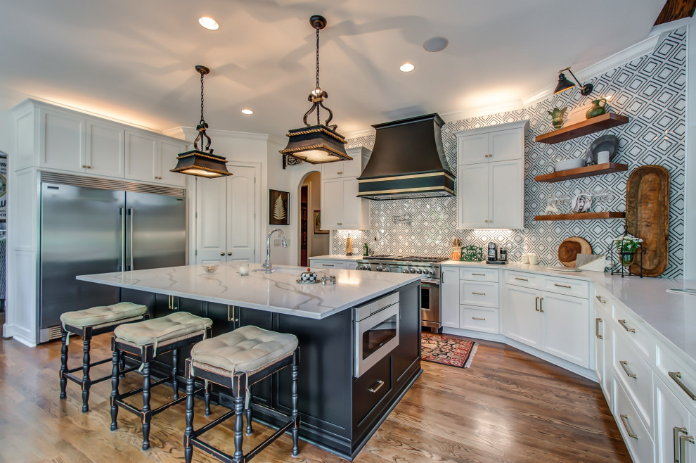 Transitional u-shaped kitchen in Nashville with an undermount sink, beaded inset cabinets, white cabinets, multi-coloured splashback, stainless steel appliances, medium hardwood floors, with island, brown floor and white benchtop.