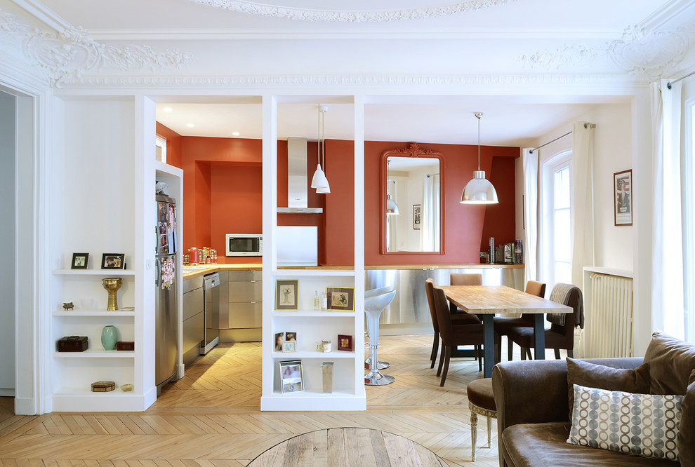 This is an example of a mid-sized contemporary l-shaped eat-in kitchen in Paris with light hardwood floors, a drop-in sink, flat-panel cabinets, stainless steel cabinets, wood benchtops, red splashback, stainless steel appliances and with island.