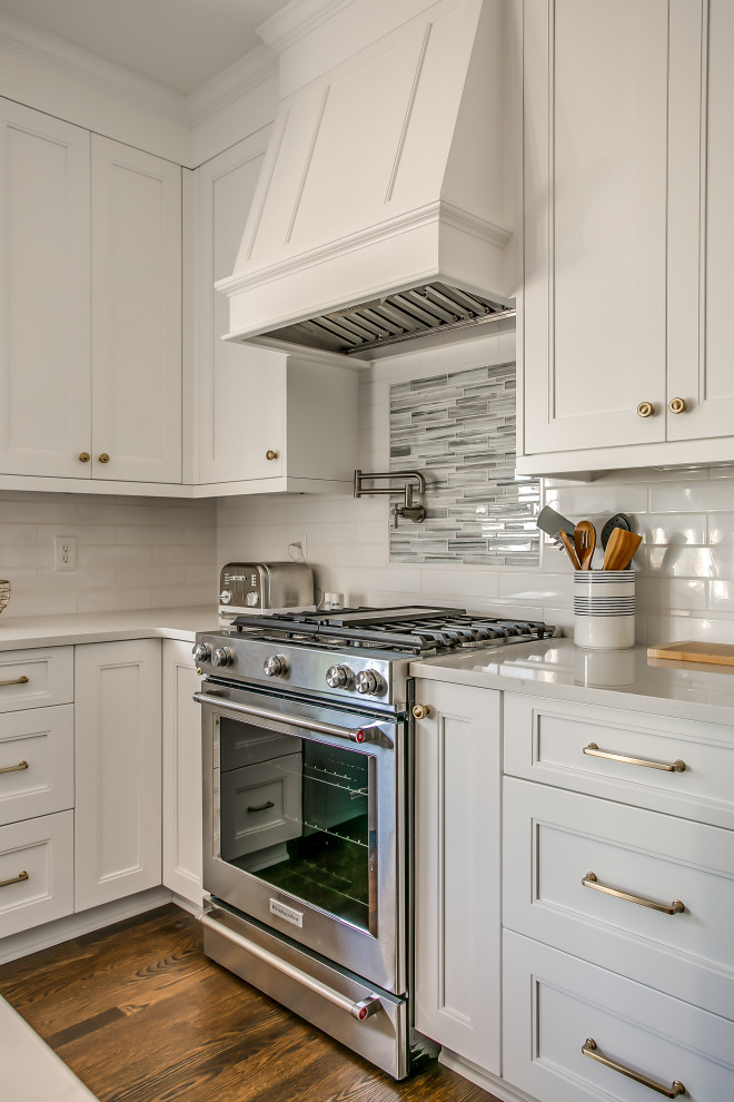 Inspiration for a transitional u-shaped kitchen in Nashville with an undermount sink, shaker cabinets, white cabinets, white splashback, ceramic splashback, stainless steel appliances, dark hardwood floors, with island, brown floor and white benchtop.