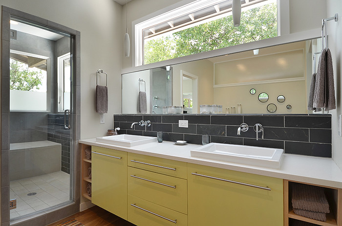 Design ideas for a mid-sized modern master bathroom in Austin with flat-panel cabinets, yellow cabinets, an alcove tub, an alcove shower, a two-piece toilet, gray tile, porcelain tile, grey walls, dark hardwood floors, a vessel sink, solid surface benchtops, brown floor and a hinged shower door.