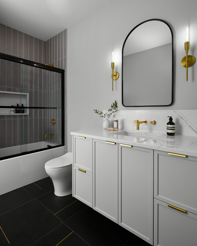 Photo of a mid-sized modern kids bathroom in Chicago with shaker cabinets, grey cabinets, a drop-in tub, a shower/bathtub combo, gray tile, ceramic tile, grey walls, porcelain floors, engineered quartz benchtops, black floor, a sliding shower screen, white benchtops, a single vanity and a built-in vanity.