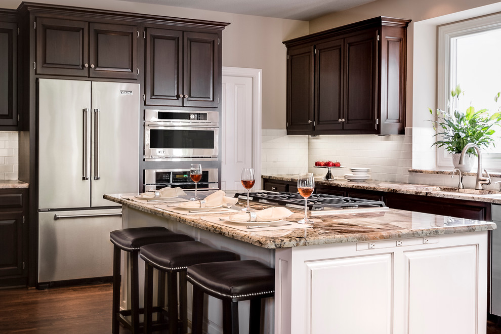 Mid-sized transitional u-shaped medium tone wood floor open concept kitchen photo in Kansas City with a drop-in sink, recessed-panel cabinets, dark wood cabinets, granite countertops, white backsplash, subway tile backsplash, stainless steel appliances and an island