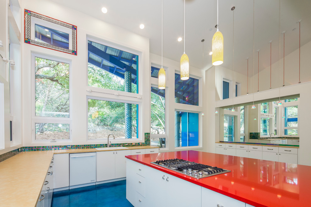 This is an example of a mid-sized eclectic u-shaped eat-in kitchen in Austin with a double-bowl sink, flat-panel cabinets, white cabinets, multi-coloured splashback, glass tile splashback, white appliances, concrete floors and with island.