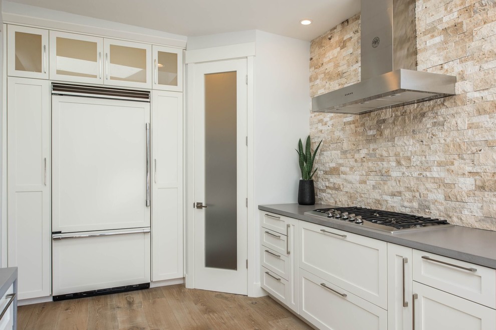 Large transitional u-shaped light wood floor open concept kitchen photo in Orange County with shaker cabinets, white cabinets, stone tile backsplash, no island, beige backsplash, stainless steel appliances and gray countertops