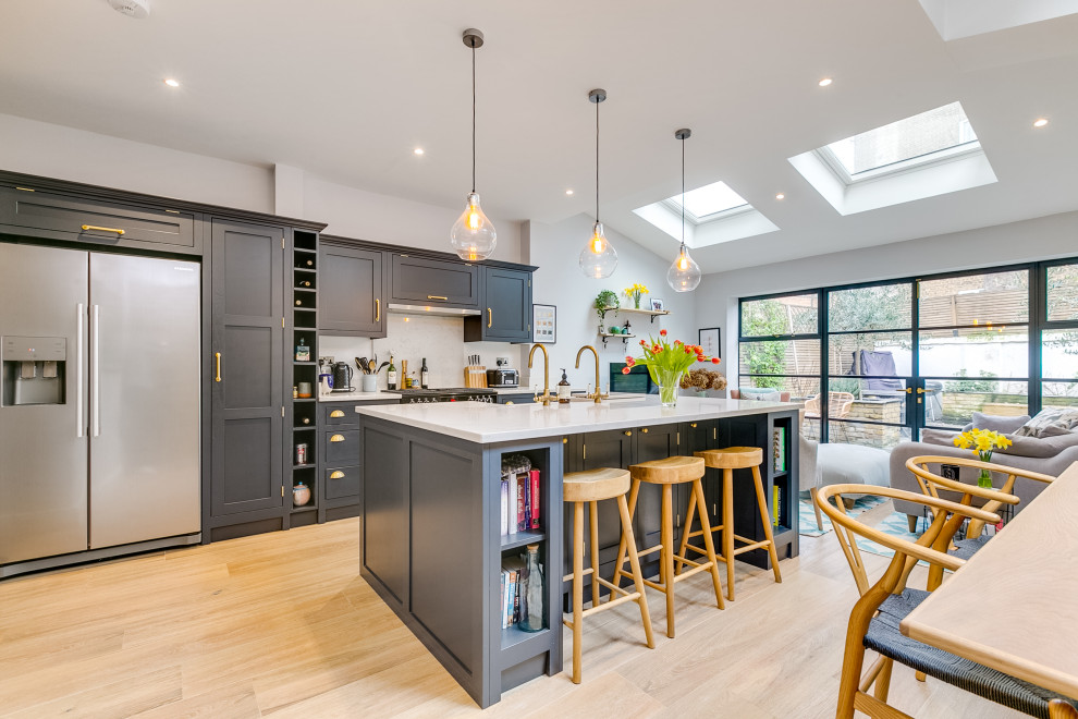 Design ideas for a mid-sized transitional galley eat-in kitchen in London with a drop-in sink, beige splashback, with island, shaker cabinets, grey cabinets, quartz benchtops, stainless steel appliances, light hardwood floors, beige floor and white benchtop.