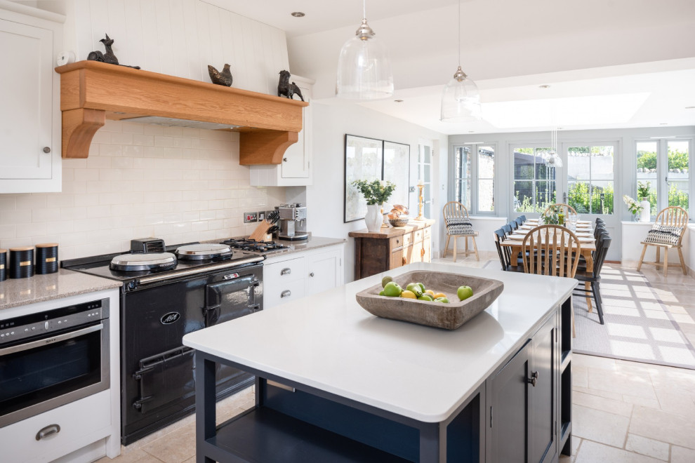 This is an example of a country eat-in kitchen in Other with limestone floors, with island, beige floor, shaker cabinets, white cabinets, white splashback, subway tile splashback, black appliances and grey benchtop.