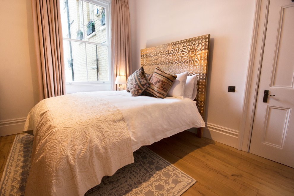 This is an example of a mid-sized traditional guest bedroom in London with white walls, light hardwood floors, no fireplace and beige floor.