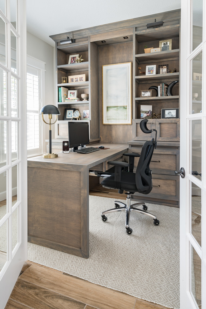 This is an example of a transitional home office in Tampa with white walls, light hardwood floors, a built-in desk and brown floor.