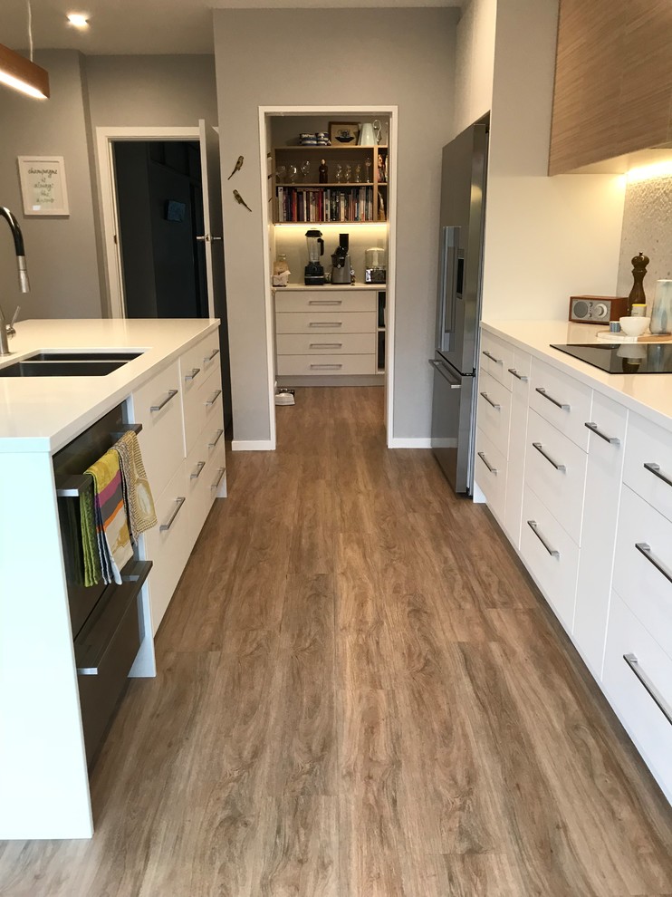 Inspiration for a large scandinavian galley separate kitchen in Christchurch with a double-bowl sink, flat-panel cabinets, white cabinets, quartz benchtops, grey splashback, porcelain splashback, stainless steel appliances, with island, brown floor and vinyl floors.