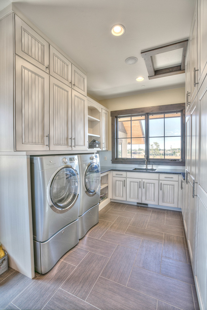 Design ideas for an expansive country u-shaped dedicated laundry room in Denver with an undermount sink, white cabinets, solid surface benchtops, beige walls, slate floors, a side-by-side washer and dryer and recessed-panel cabinets.