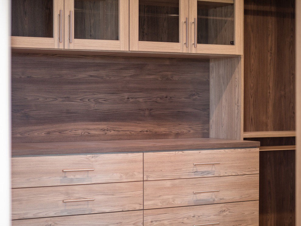 Modelo de armario vestidor unisex actual de tamaño medio con armarios con paneles lisos, puertas de armario de madera oscura, suelo de madera clara y suelo beige