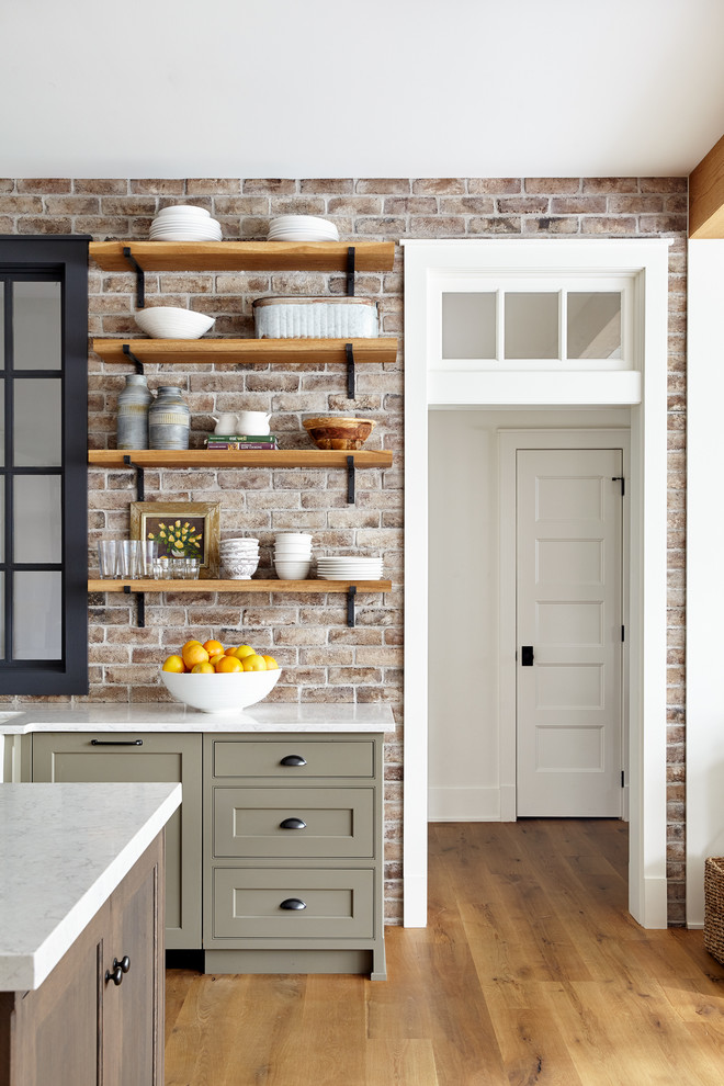 Design ideas for a large country l-shaped open plan kitchen in Philadelphia with a farmhouse sink, shaker cabinets, white cabinets, quartz benchtops, red splashback, brick splashback, panelled appliances, light hardwood floors, with island and grey benchtop.