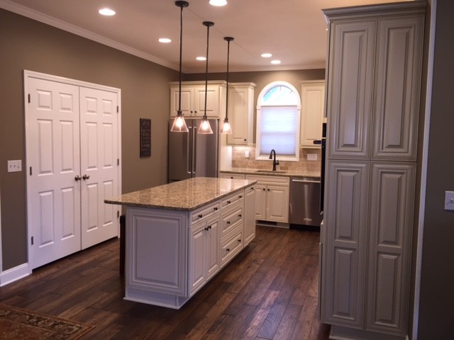 Kitchen - mid-sized transitional l-shaped dark wood floor kitchen idea with an undermount sink, raised-panel cabinets, white cabinets, granite countertops, beige backsplash, stone tile backsplash, stainless steel appliances and an island