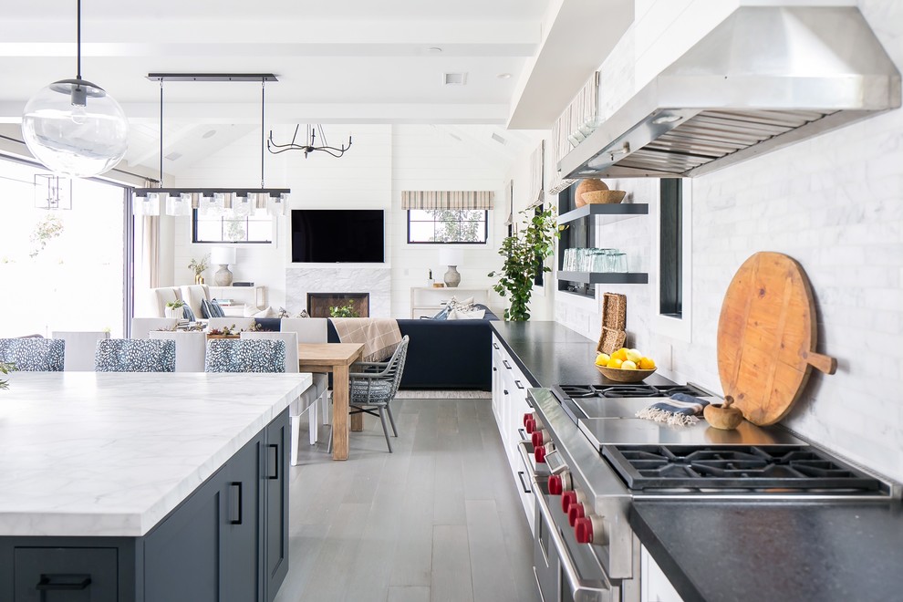This is an example of a large transitional open plan kitchen in Orange County with shaker cabinets, white cabinets, marble benchtops, grey splashback, marble splashback, stainless steel appliances, medium hardwood floors, with island and grey floor.