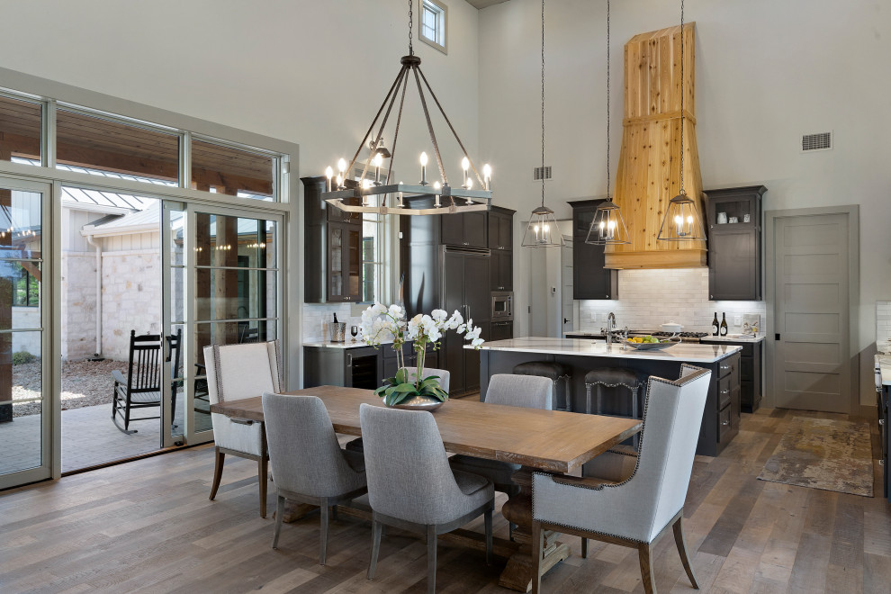 Inspiration for a large country u-shaped eat-in kitchen in Austin with light hardwood floors, grey floor, wood, a farmhouse sink, shaker cabinets, black cabinets, quartzite benchtops, white splashback, porcelain splashback, panelled appliances, with island and white benchtop.