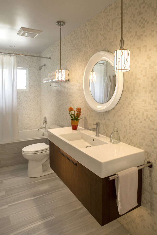 Inspiration for a mid-sized contemporary bathroom in Other with flat-panel cabinets, medium wood cabinets, a drop-in tub, a shower/bathtub combo, a one-piece toilet, white tile, white walls, porcelain floors and an integrated sink.