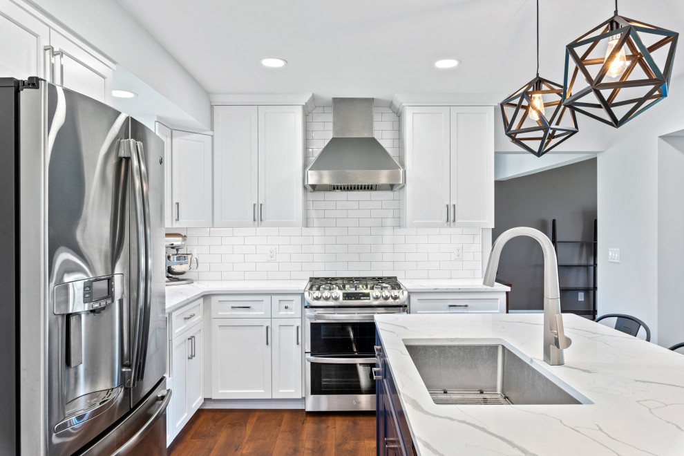Design ideas for a mid-sized transitional kitchen in Milwaukee with an undermount sink, recessed-panel cabinets, white cabinets, quartz benchtops, white splashback, subway tile splashback, stainless steel appliances, vinyl floors, with island, brown floor and white benchtop.