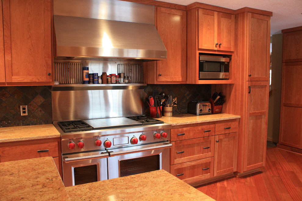This is an example of a mid-sized traditional galley eat-in kitchen in Minneapolis with a double-bowl sink, shaker cabinets, dark wood cabinets, granite benchtops, multi-coloured splashback, stone tile splashback, stainless steel appliances, dark hardwood floors, a peninsula, red floor and brown benchtop.