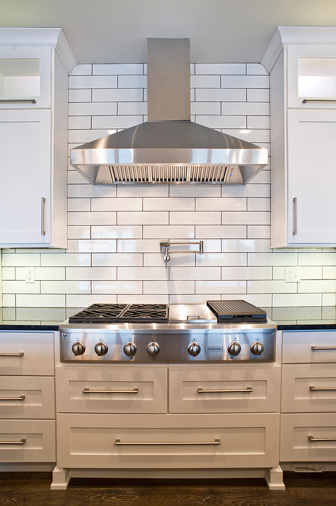 Large transitional l-shaped dark wood floor and brown floor eat-in kitchen photo with an undermount sink, white cabinets, granite countertops, white backsplash, subway tile backsplash, stainless steel appliances, an island and shaker cabinets