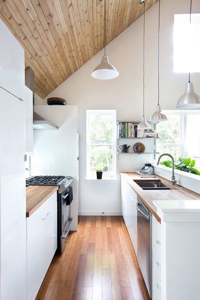 This is an example of a small scandinavian galley kitchen in London with a double-bowl sink, flat-panel cabinets, white cabinets, wood benchtops, stainless steel appliances, medium hardwood floors and no island.