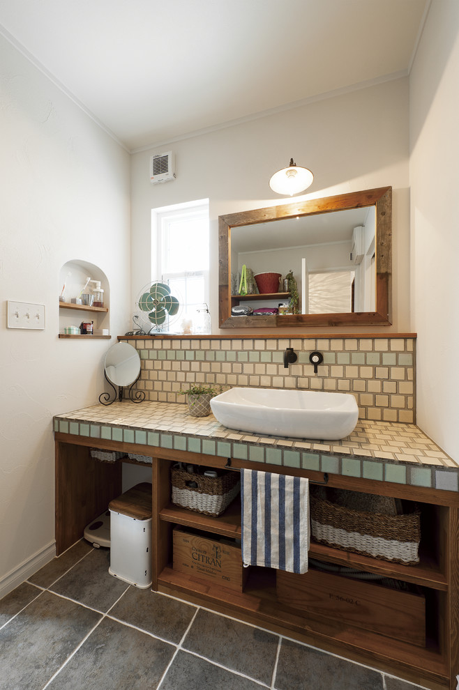 Inspiration for a country powder room in Other with open cabinets, green tile, beige tile, blue tile, white walls, a vessel sink, tile benchtops and black floor.