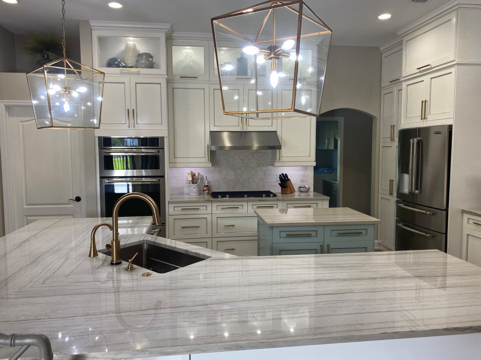 Mid-sized transitional l-shaped eat-in kitchen in Tampa with an undermount sink, shaker cabinets, white cabinets, quartzite benchtops, white splashback, stone tile splashback, stainless steel appliances, vinyl floors, multiple islands, brown floor and white benchtop.