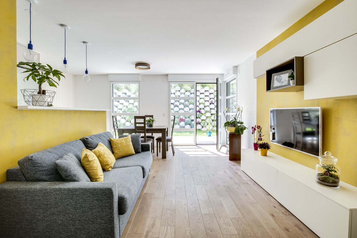 Inspiration for a mid-sized contemporary open concept family room in Paris with yellow walls, light hardwood floors, a wall-mounted tv, no fireplace and brown floor.