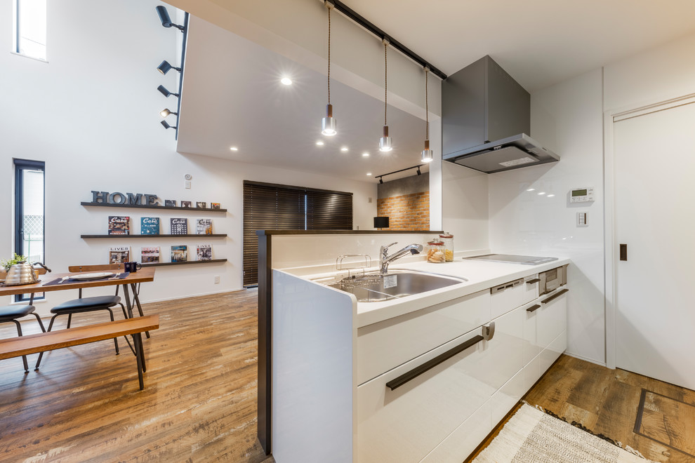 Photo of an industrial galley open plan kitchen in Tokyo Suburbs with a single-bowl sink, flat-panel cabinets, white cabinets, white splashback, medium hardwood floors, with island and brown floor.