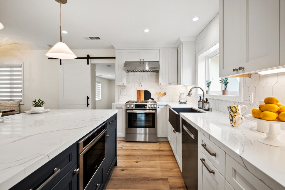 This is an example of a large l-shaped eat-in kitchen in San Francisco with a farmhouse sink, shaker cabinets, white cabinets, quartzite benchtops, white splashback, porcelain splashback, stainless steel appliances, vinyl floors, with island, brown floor and white benchtop.