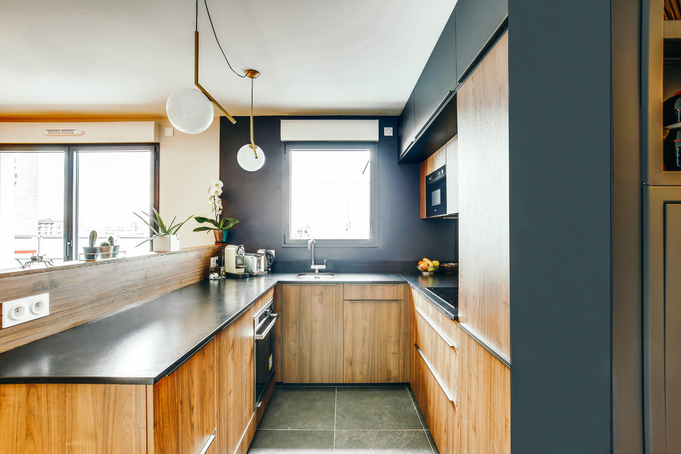 Small contemporary u-shaped open plan kitchen in Paris with an undermount sink, medium wood cabinets, granite benchtops, black splashback, panelled appliances, ceramic floors, black benchtop, flat-panel cabinets, a peninsula and grey floor.