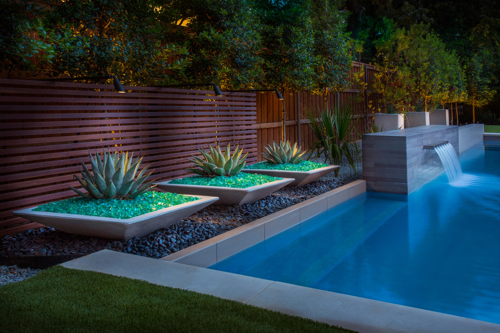 This is an example of a mid-sized modern backyard rectangular pool in Dallas with a water feature and decking.