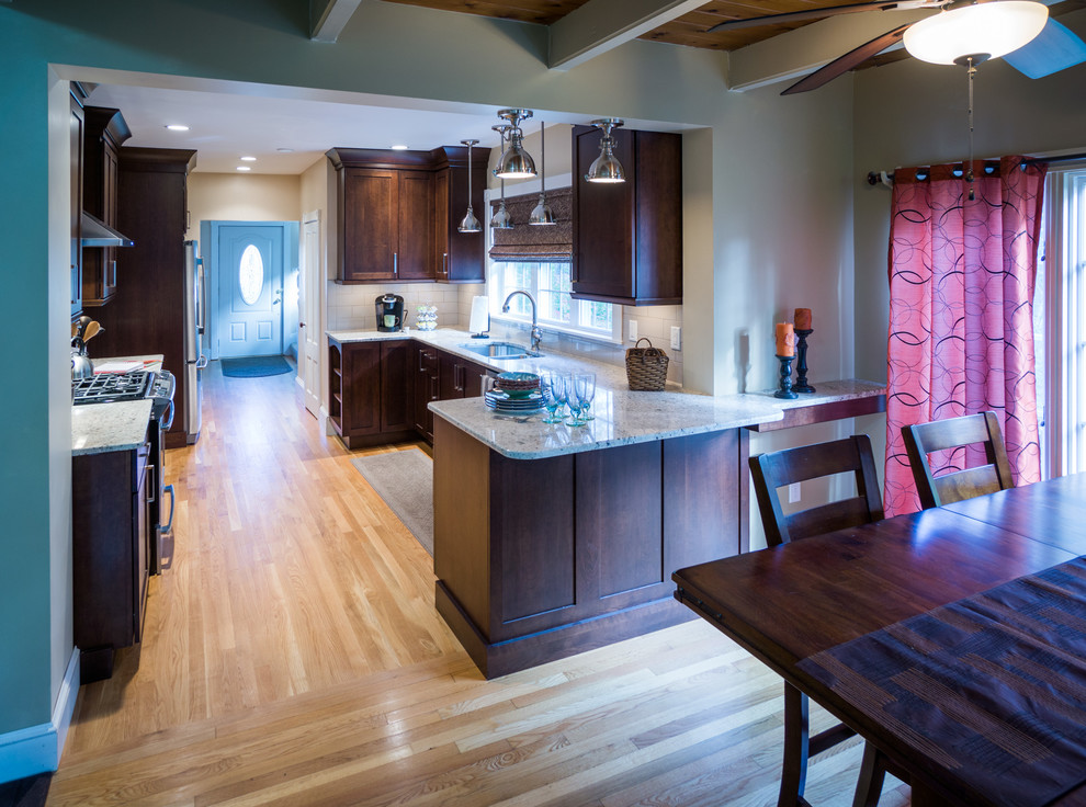 Photo of a large transitional u-shaped eat-in kitchen in Providence with a peninsula, shaker cabinets, dark wood cabinets, granite benchtops, beige splashback, ceramic splashback, stainless steel appliances, an undermount sink and light hardwood floors.